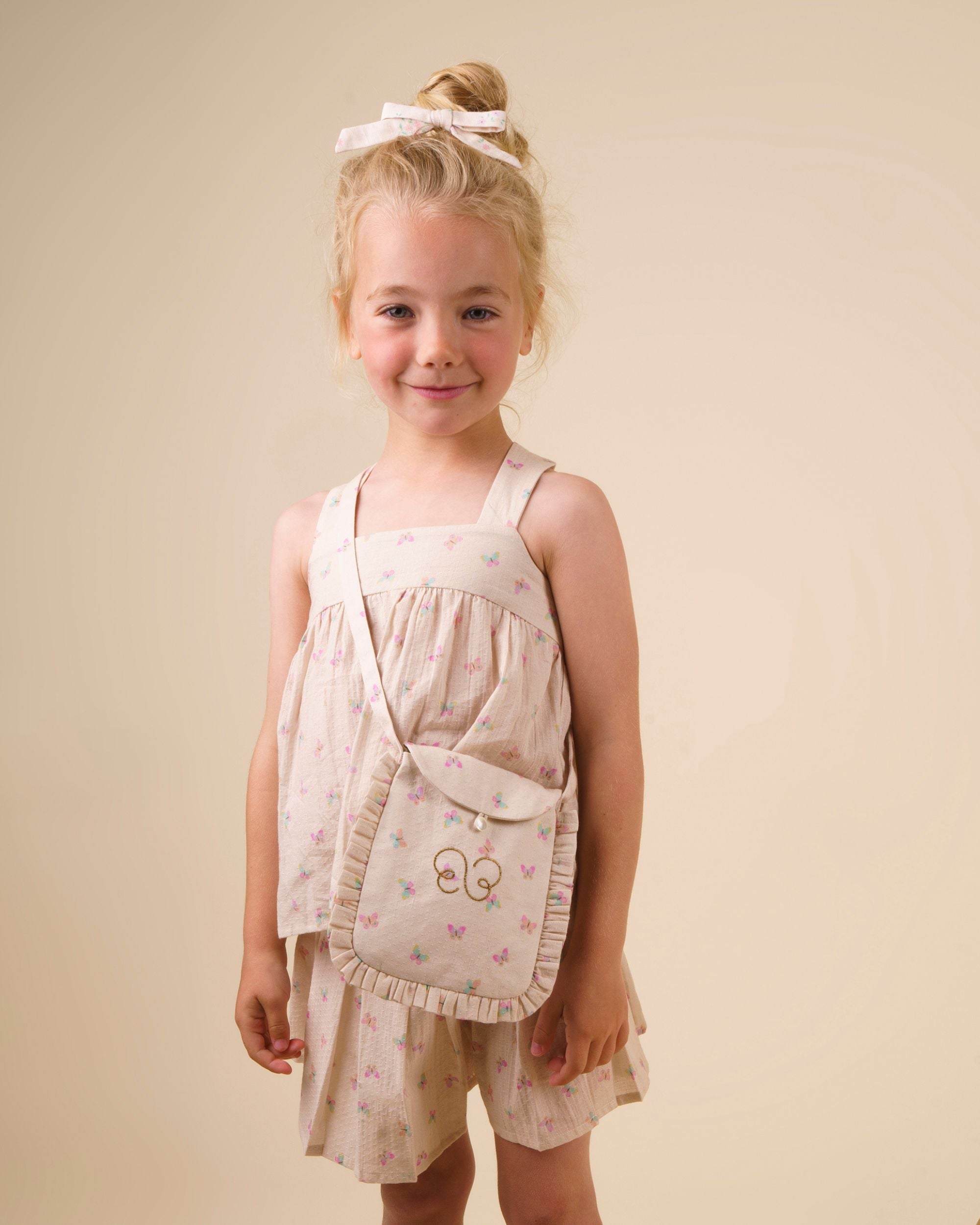 Early Sunday, Romy Blouse in Butterflies print, made from Printed Cotton Tiny Swiss Dobby fabric, featuring a sleeveless design with cross-back straps, a gathered waist & a soft flared silhouette, shown in close-up shot of a model wearing it during a studio shoot