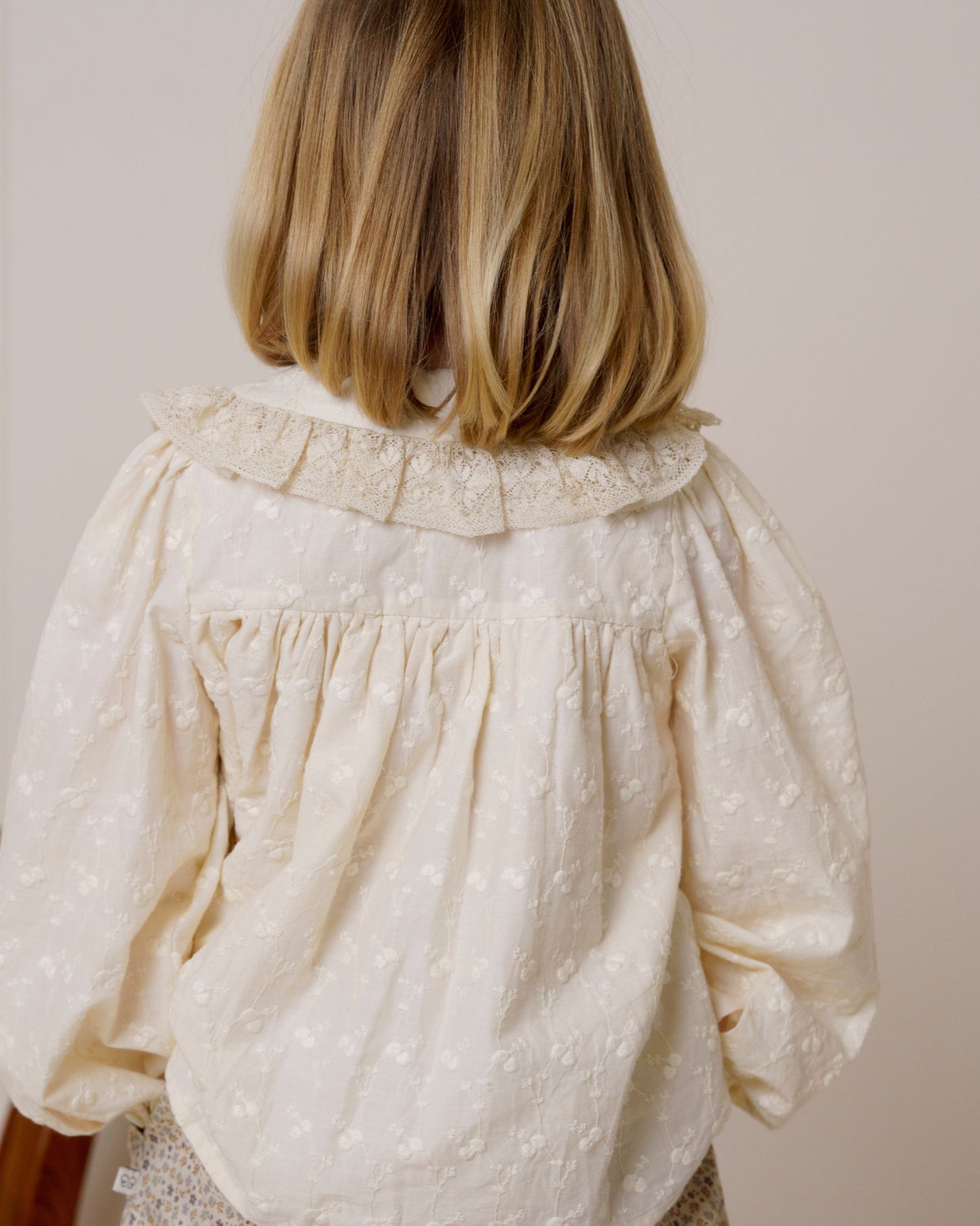 Early Sunday, Rosa Blouse in Hazelnut Cream, made from All-Over Embroidered Cotton Cambric fabric, featuring Frilled neckline detailed with a lace collar for a vintage touch, shown in a back view of model wearing it