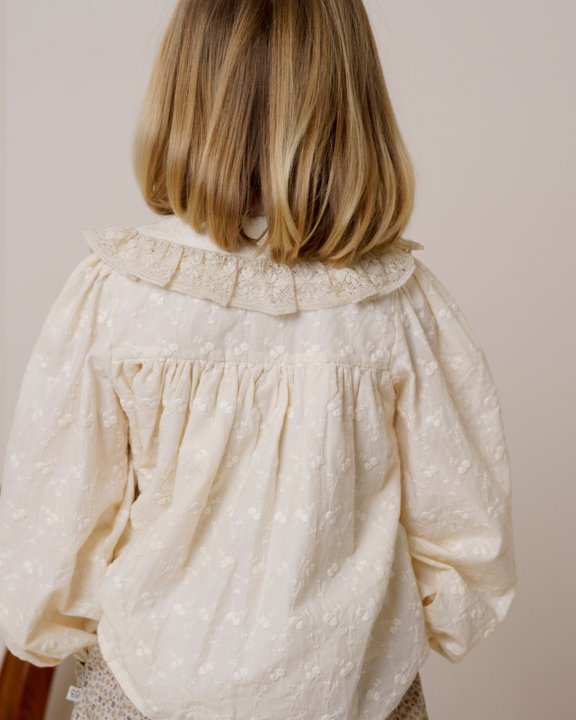 Early Sunday, Rosa Blouse in Hazelnut Cream, made from All-Over Embroidered Cotton Cambric fabric, featuring Frilled neckline detailed with a lace collar for a vintage touch, shown in a back view of model wearing it