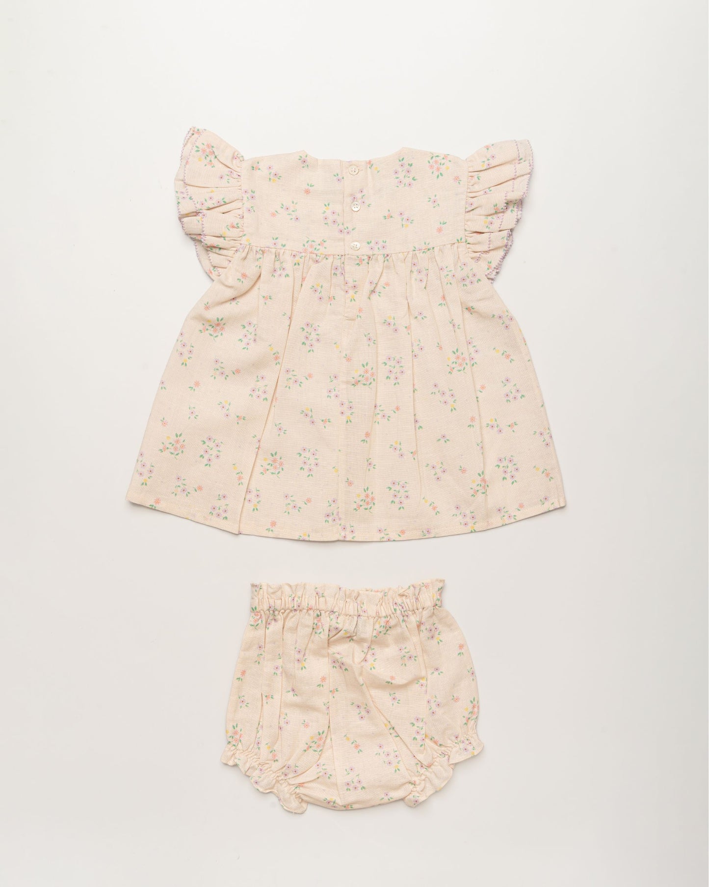 Early Sunday, Sienna Baby Dress & Bloomer Set in Painted Bouquet print, made from 70% Cotton 30% Linen fabric, featuring a relaxed fit with smocked chest band & frilled sleeves, shown in a back flat-lay view