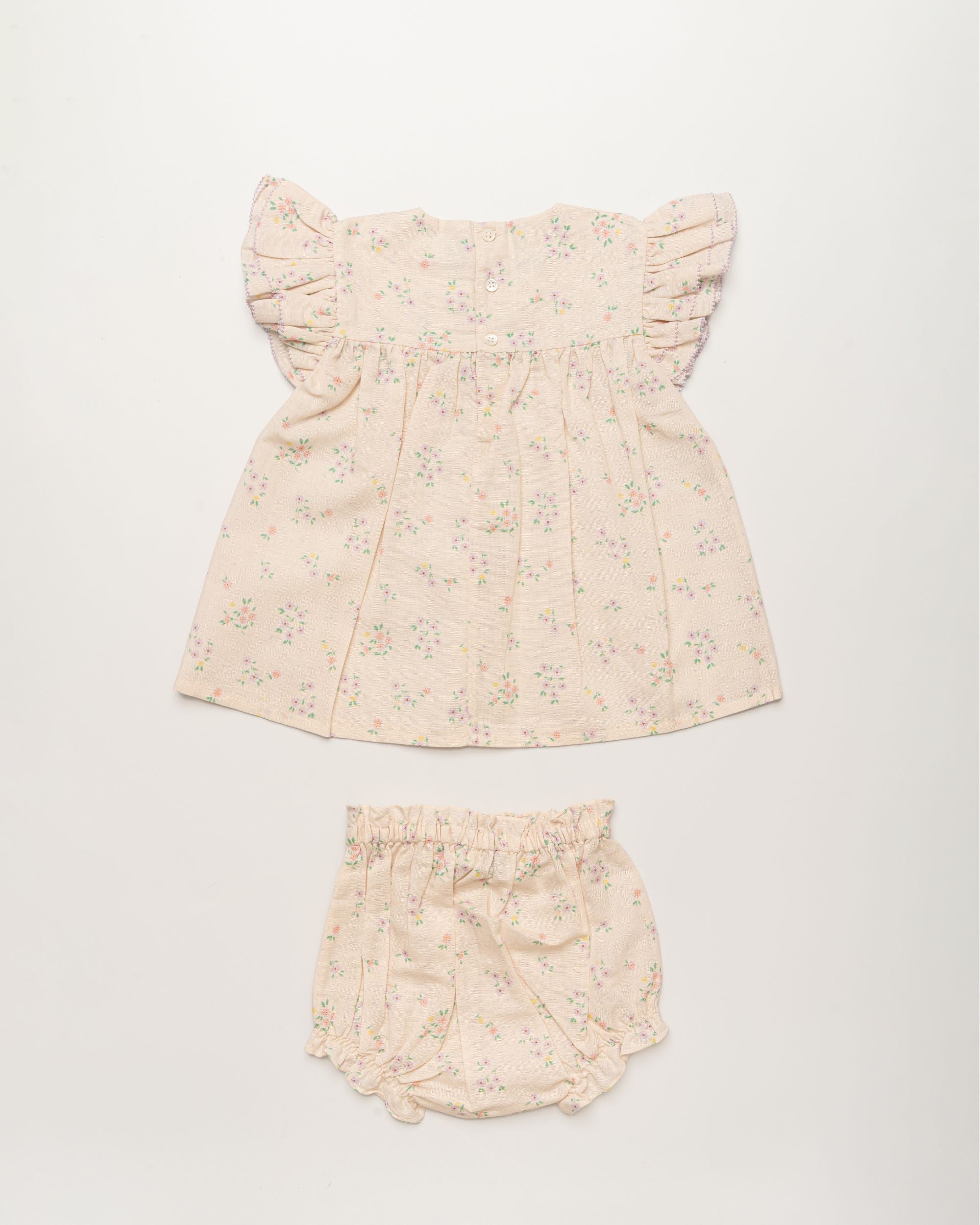 Early Sunday, Sienna Baby Dress & Bloomer Set in Painted Bouquet print, made from 70% Cotton 30% Linen fabric, featuring a relaxed fit with smocked chest band & frilled sleeves, shown in a back flat-lay view