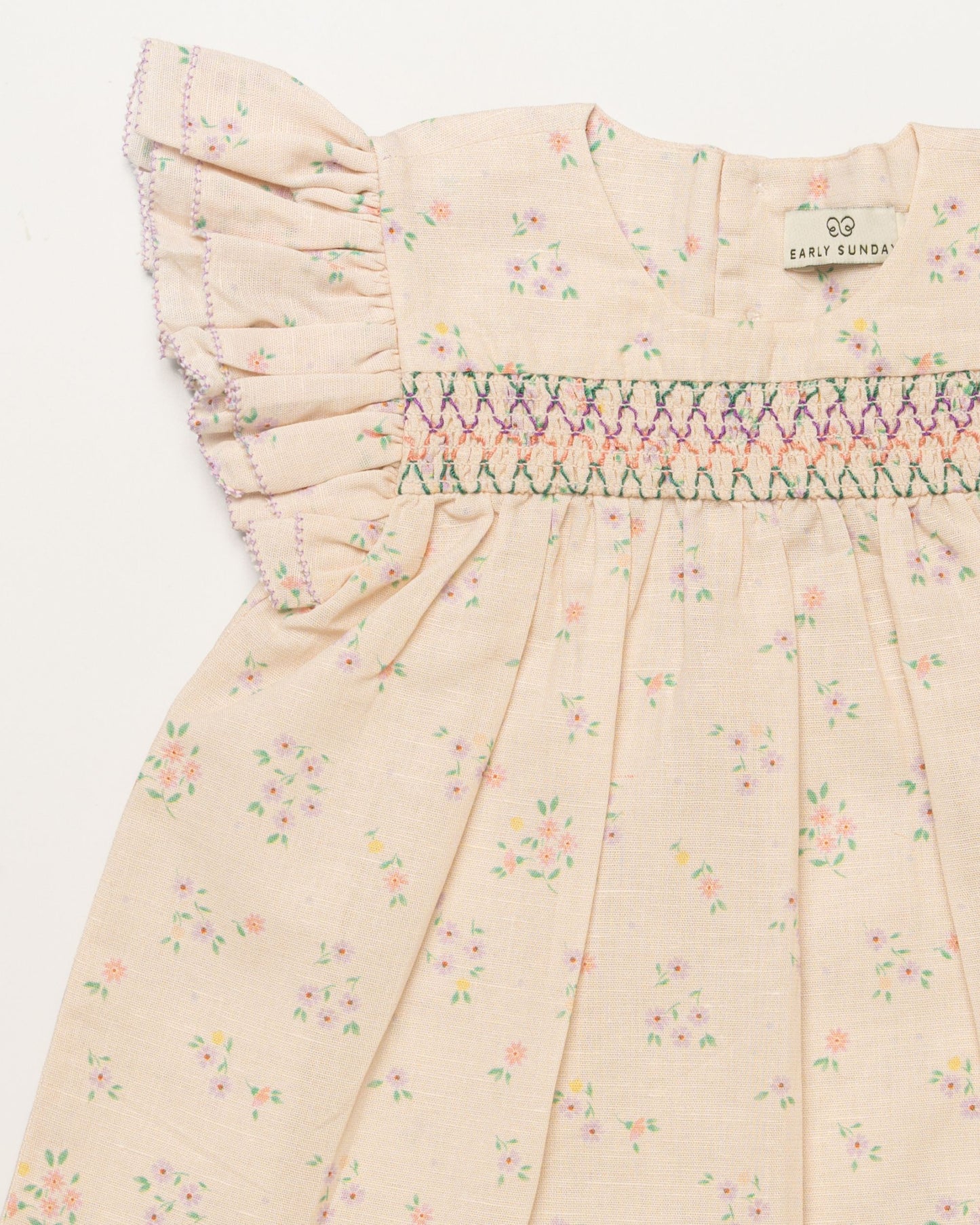 Early Sunday, Sienna Baby Dress & Bloomer Set in Painted Bouquet print, made from 70% Cotton 30% Linen fabric, featuring a relaxed fit with smocked chest band & frilled sleeves, shown in a closeup flat-lay view