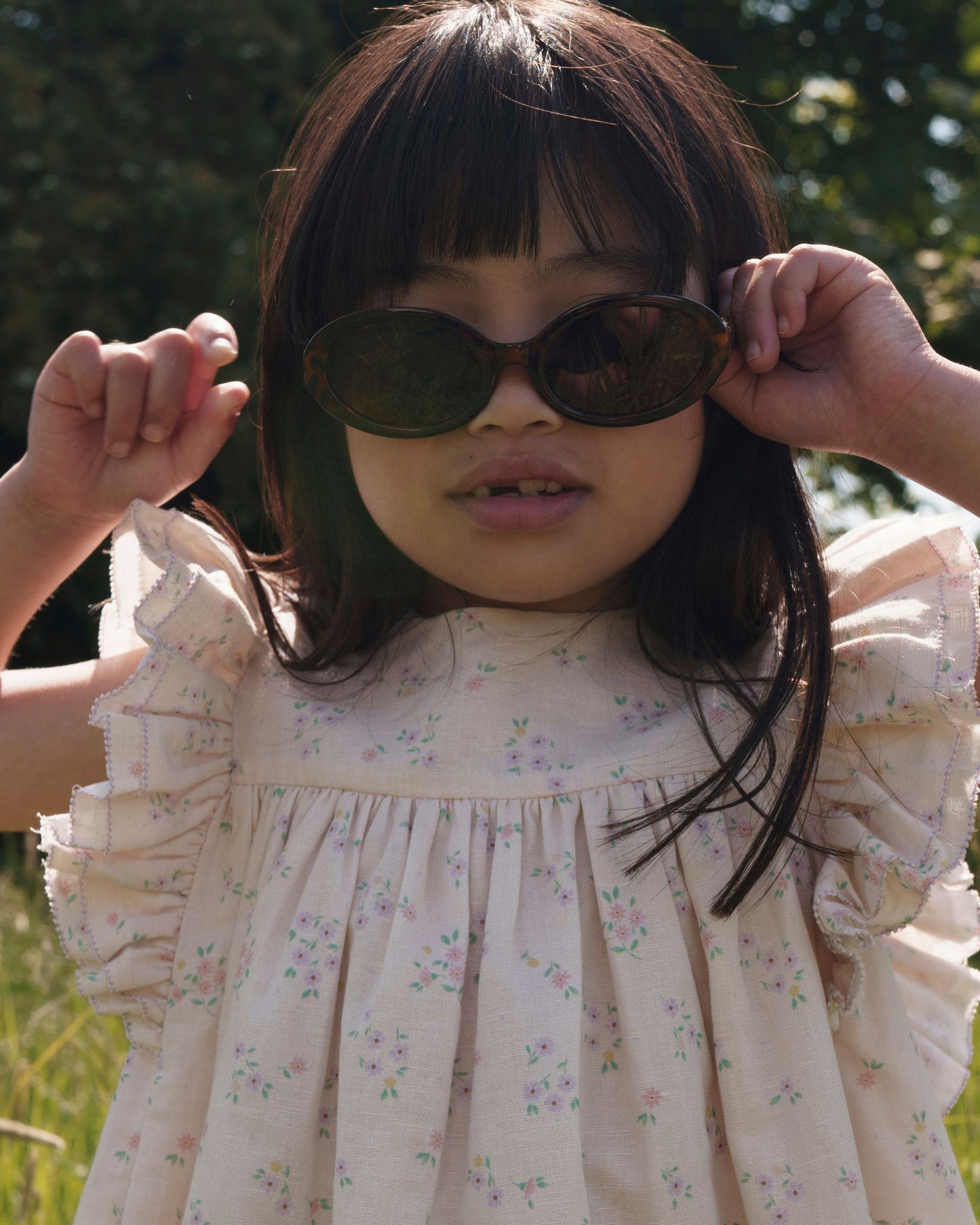 Early Sunday, Sita Dress in Painted Bouquet print, made from 70% Cotton 30% Linen fabric, featuring a sleeveless design with wide shoulder straps & a delicate lace yoke, shown in a close up shot of model playing outdoors