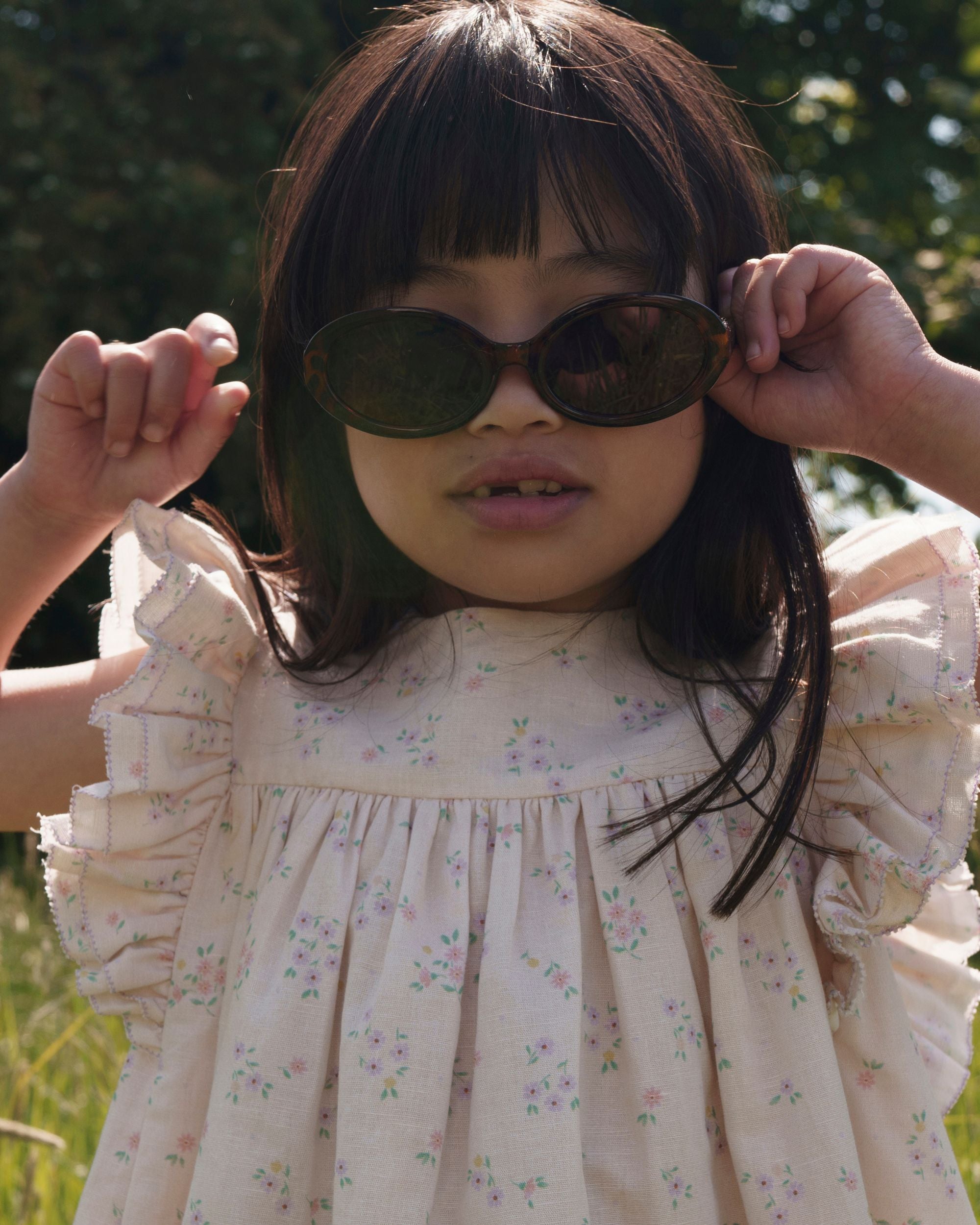 Early Sunday, Sita Dress in Painted Bouquet print, made from 70% Cotton 30% Linen fabric, featuring a sleeveless design with wide shoulder straps & a delicate lace yoke, shown in a close up shot of model playing outdoors