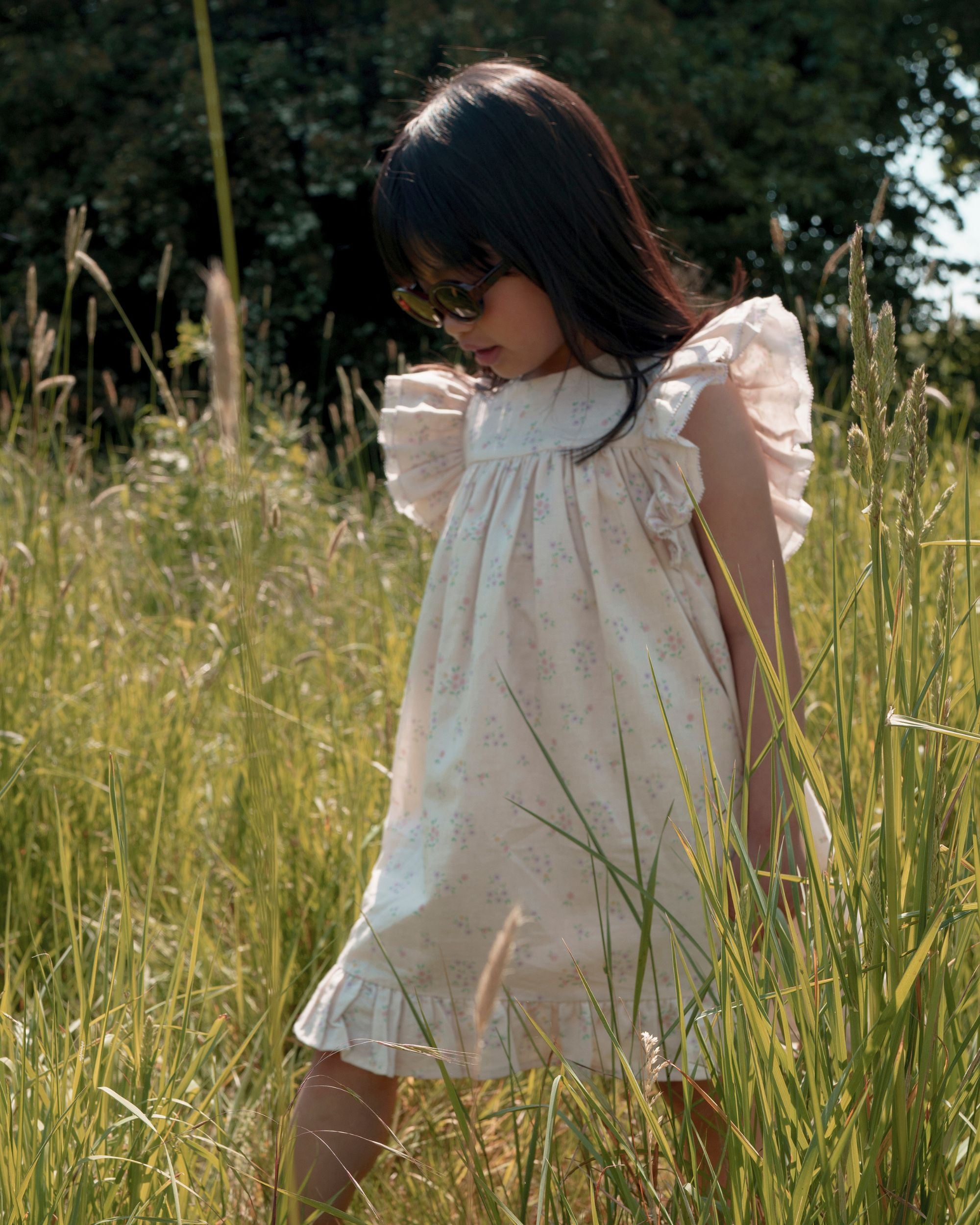 Early Sunday, Sita Dress in Painted Bouquet print, made from 70% Cotton 30% Linen fabric, featuring a sleeveless design with wide shoulder straps & a delicate lace yoke, shown in an angled view of a model wearing outdoors