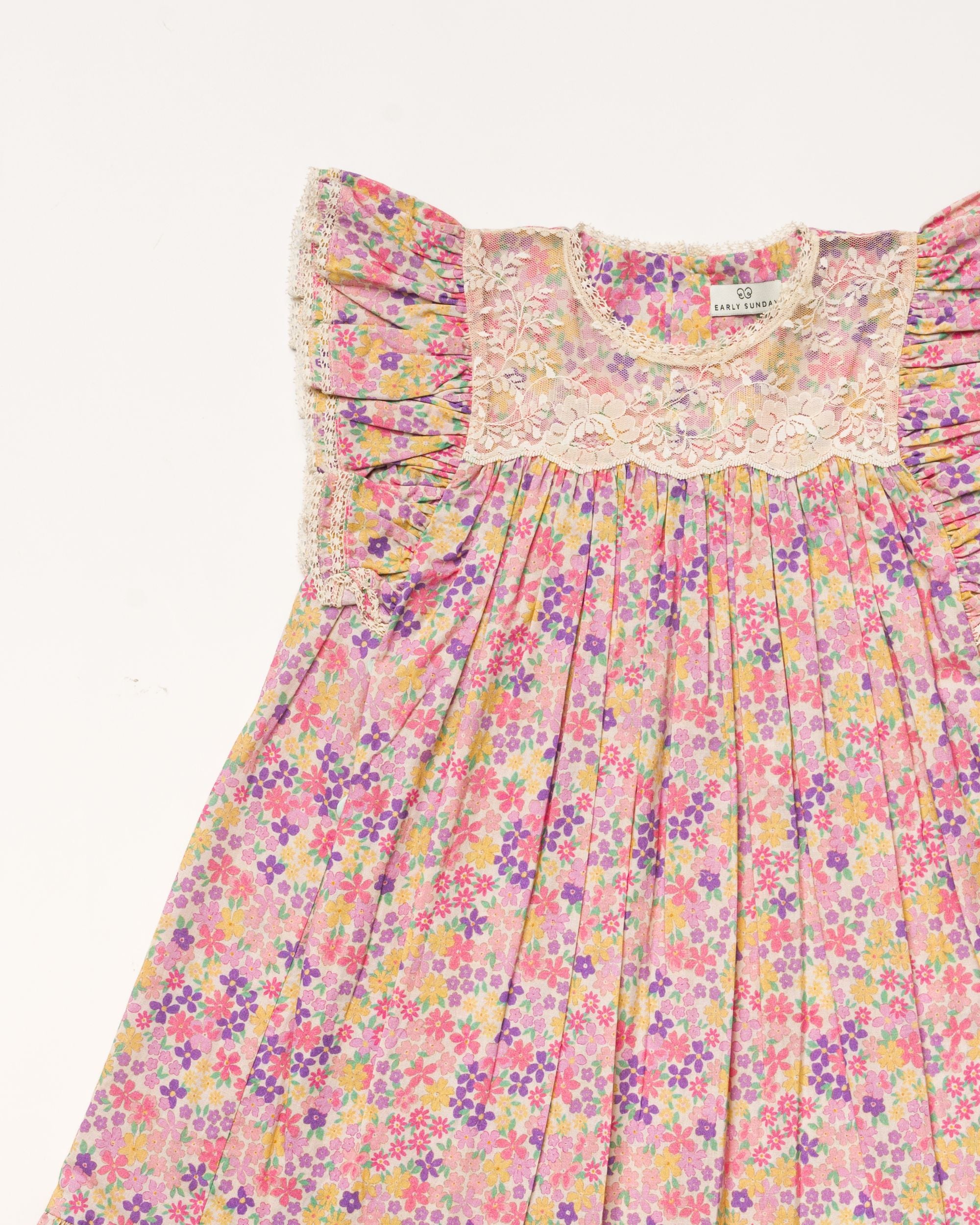 Early Sunday, Sita Dress in Emma Floral Purple color, made from Organic Printed Cotton Cambric fabric, featuring a sleeveless design with wide shoulder straps & a delicate lace yoke, shown in a closeup flat-lay view