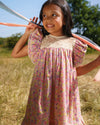 Early Sunday, Sita Dress in Emma Floral Purple color, made from Organic Printed Cotton Cambric fabric, featuring a sleeveless design with wide shoulder straps & a delicate lace yoke, shown in a close up shot of model playing outdoors