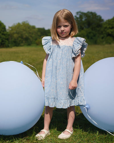Early Sunday, Sita Dress in Tonal Floral Blue color, made from Printed Cotton Tiny Swiss Dobby fabric, featuring a sleeveless design with wide shoulder straps & a delicate lace yoke, shown in a close up shot of model playing outdoors