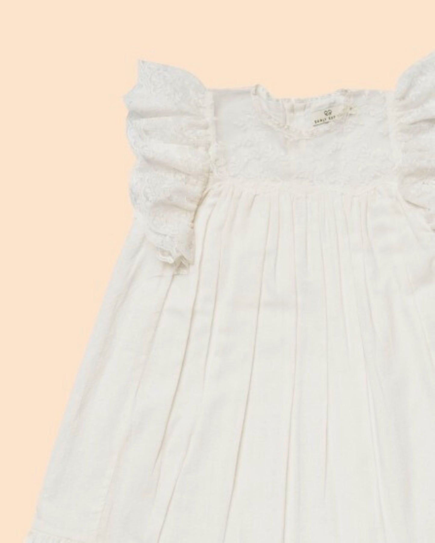 Early Sunday, Sita Dress in Ivory color, made from Tiny Swiss Dobby fabric, featuring a sleeveless design with wide shoulder straps & a delicate lace yoke, shown in a closeup flat-lay view
