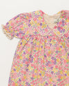 Early Sunday, Sofia Baby Dress & Bloomer Set in Emma Floral Purple color, made from 100% Organic Cotton 60s Cambric fabric, featuring short sleeves with peter pan collar, shown in a closeup flat-lay view