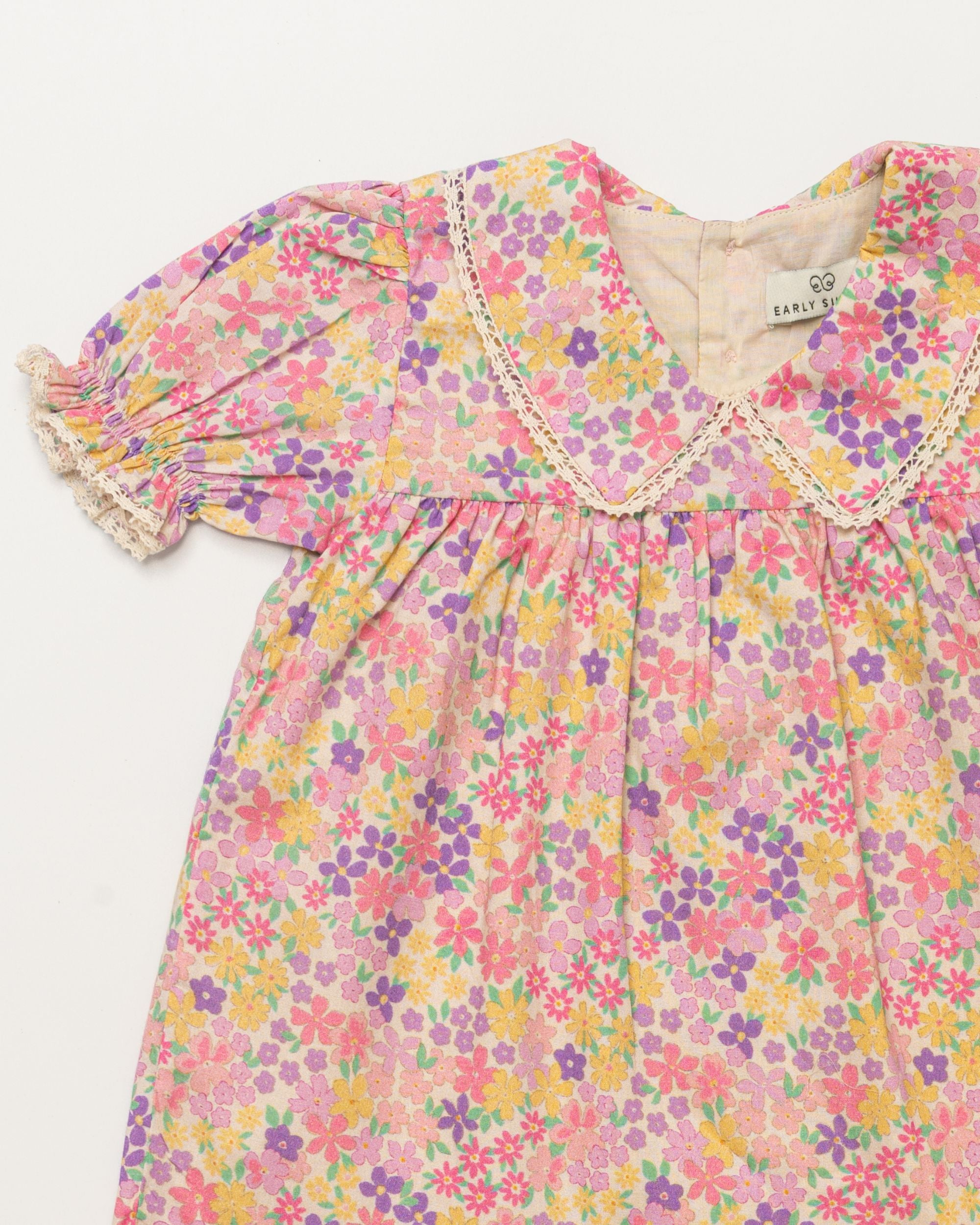 Early Sunday, Sofia Baby Dress & Bloomer Set in Emma Floral Purple color, made from 100% Organic Cotton 60s Cambric fabric, featuring short sleeves with peter pan collar, shown in a closeup flat-lay view
