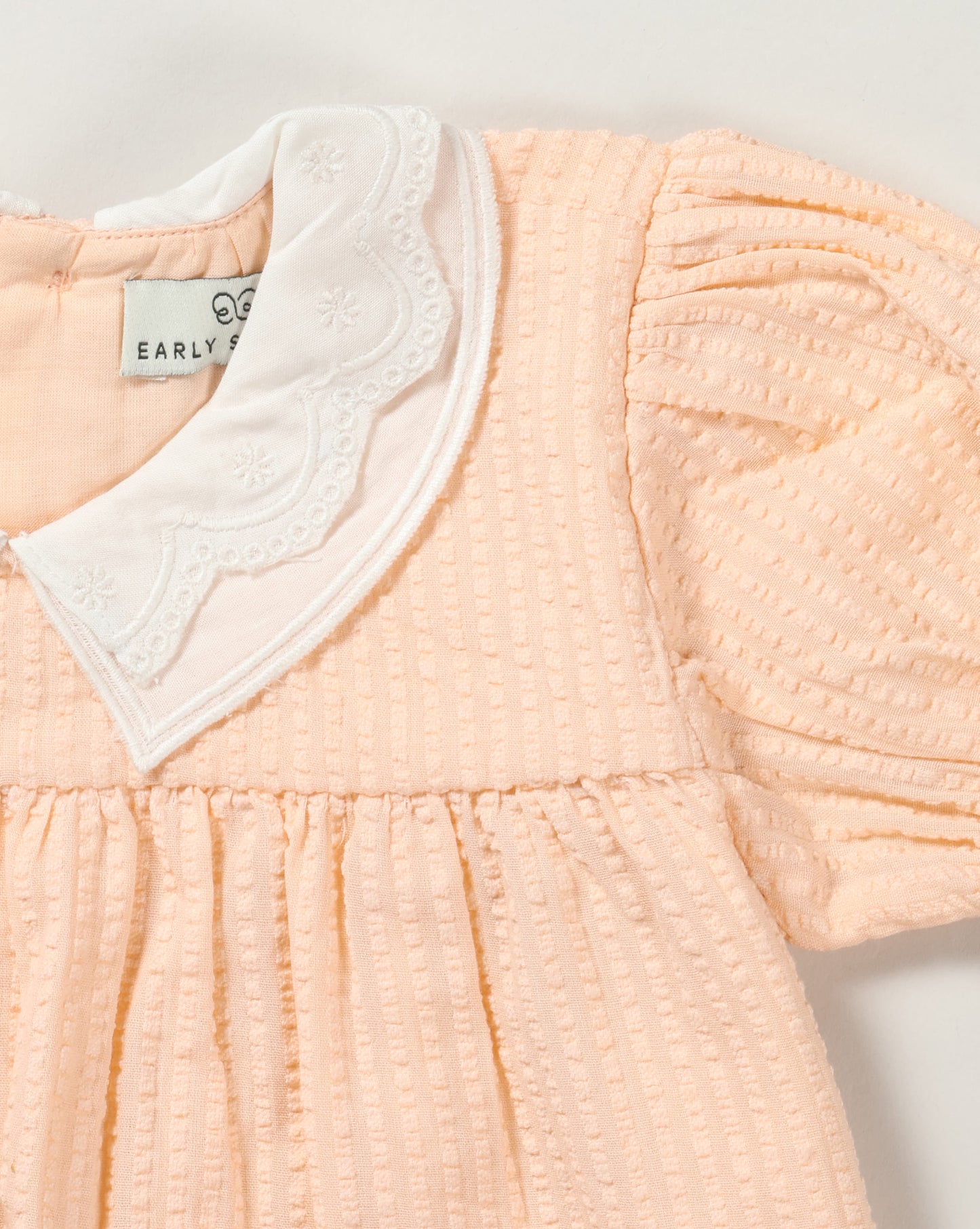 Early Sunday, Sukie Baby Dress & Bloomer in Warm Sand color, made from Cotton Seersucker fabric, featuring flared dress with a relaxed fit for ease of movement, matching bloomer with an elasticated waistband for comfort and flexibility., shown in a closeup flat-lay view