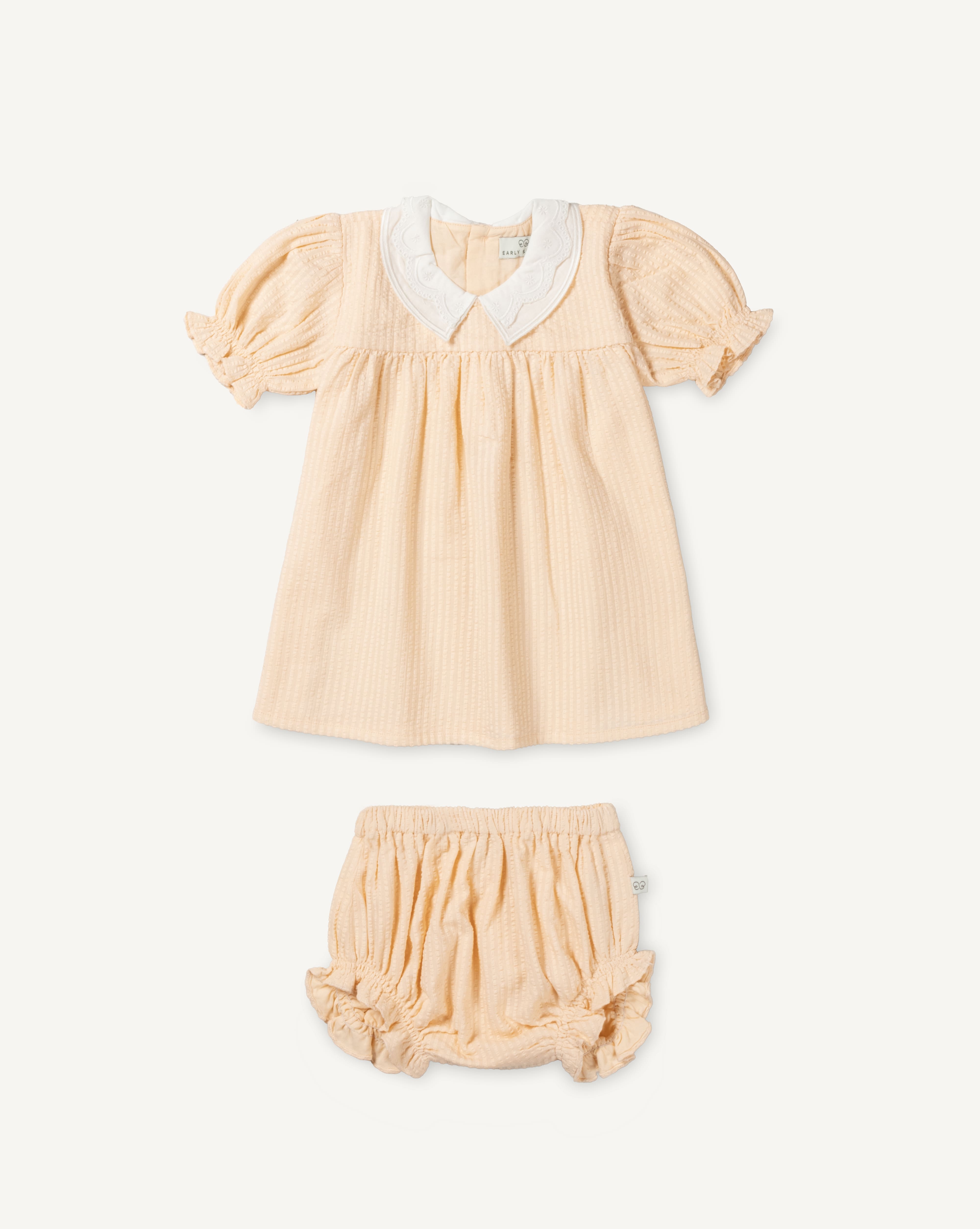 Early Sunday, Sukie Baby Dress & Bloomer in Warm Sand color, made from Cotton Seersucker fabric, featuring flared dress with a relaxed fit for ease of movement, matching bloomer with an elasticated waistband for comfort and flexibility., shown in a front flat-lay view