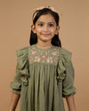 Early Sunday, Suzanne Dress in Dried Leaf, made from Cotton Double Gauze fabric, featuring classic silhouette with floral embroidery around the yoke and ruffle detailing, shown in a close-up shot of a model wearing it during a studio shoot