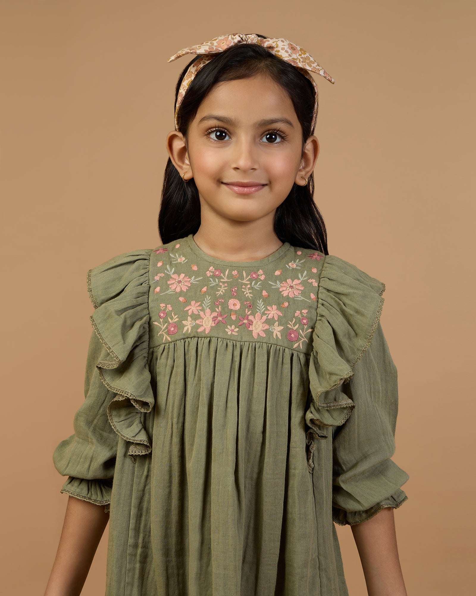 Early Sunday, Suzanne Dress in Dried Leaf, made from Cotton Double Gauze fabric, featuring classic silhouette with floral embroidery around the yoke and ruffle detailing, shown in a close-up shot of a model wearing it during a studio shoot