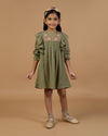 Early Sunday, Suzanne Dress in Dried Leaf, made from Cotton Double Gauze fabric, featuring classic silhouette with floral embroidery around the yoke and ruffle detailing, shown in a front view of a model wearing it in a studio setting