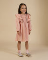 Early Sunday, Suzanne Dress in Dusty Pink, made from Cotton Double Gauze fabric, featuring classic silhouette with floral embroidery around the yoke and ruffle detailing, shown in a front view of a model wearing it in a studio setting
