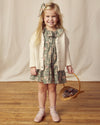 Early Sunday, Suzie Dress in Autumn Bloom Soft Green, made from Printed Cotton Double Gauze fabric, featuring classic silhouette with a ruffle neckline and mother-of-pearl buttons, shown in a front view of a model wearing it in a studio setting